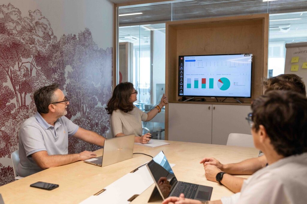 Equipe Kubs assise autour d'une table de réunion avec ses clients. Une personne de l'équipe point une présentation d'Azure sur un grand écran, au mur.