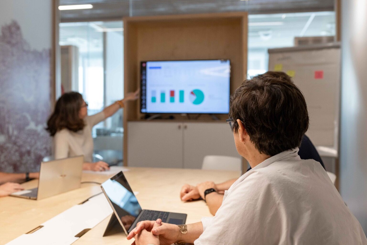 En salle de réunion, le doigt dirigé vers des éléments graphiques affichés sur grand écran, une personne de l'équipe Kubs présente à ses clients son analyse et ses recommandations stratégiques lors du rendez-vous de pilotage annuel