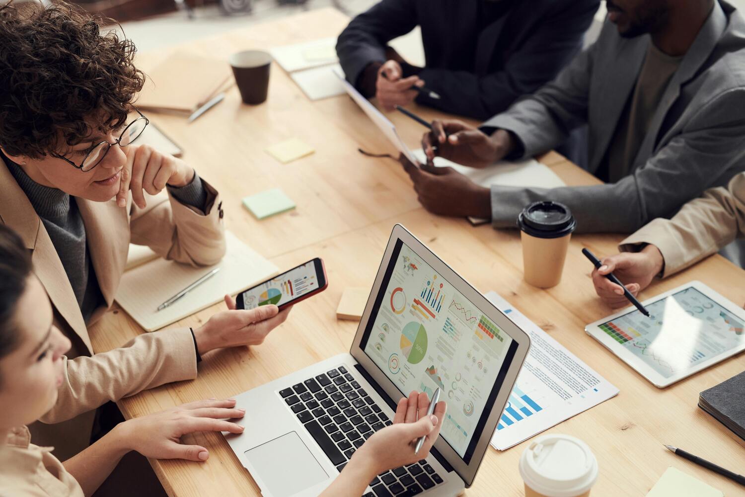 Une équipe de PME est rassemblée en réunion autour d'une table. Ils sont équipés de tablettes, smartphones et PC portables et partagent des informations sensibles liées à leur activité.