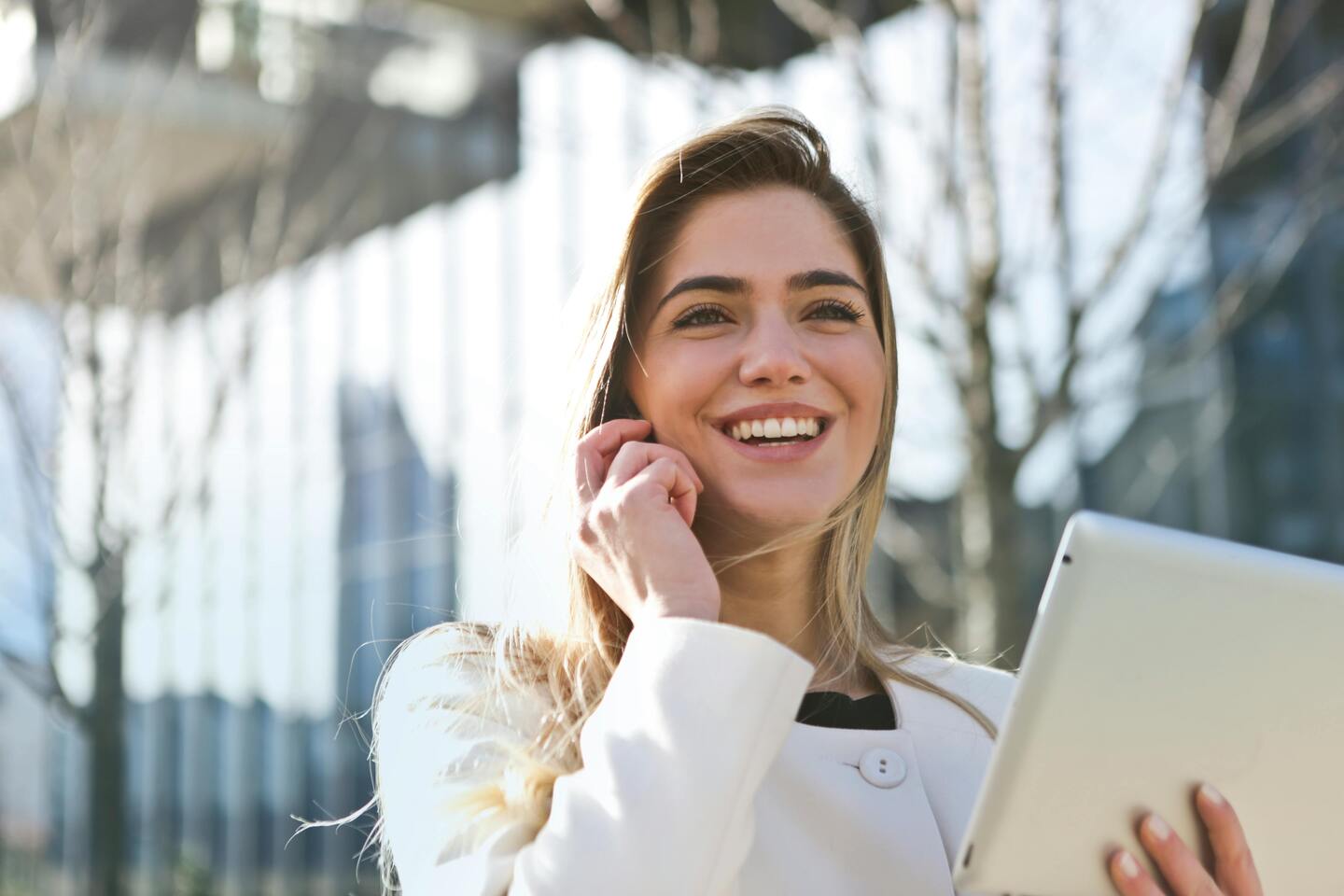 Une jeune femme dynamique et satisfaite est dans la rue avec sa tablette dans une main et son smartphone à l'oreille devant un immeuble de bureaux