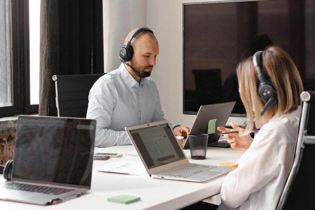 Deux techniciens sont assis à leur bureau devant leur écran d'ordinateur. Ils sont équipés de casques et micro pour échanger avec les clients au téléphone.