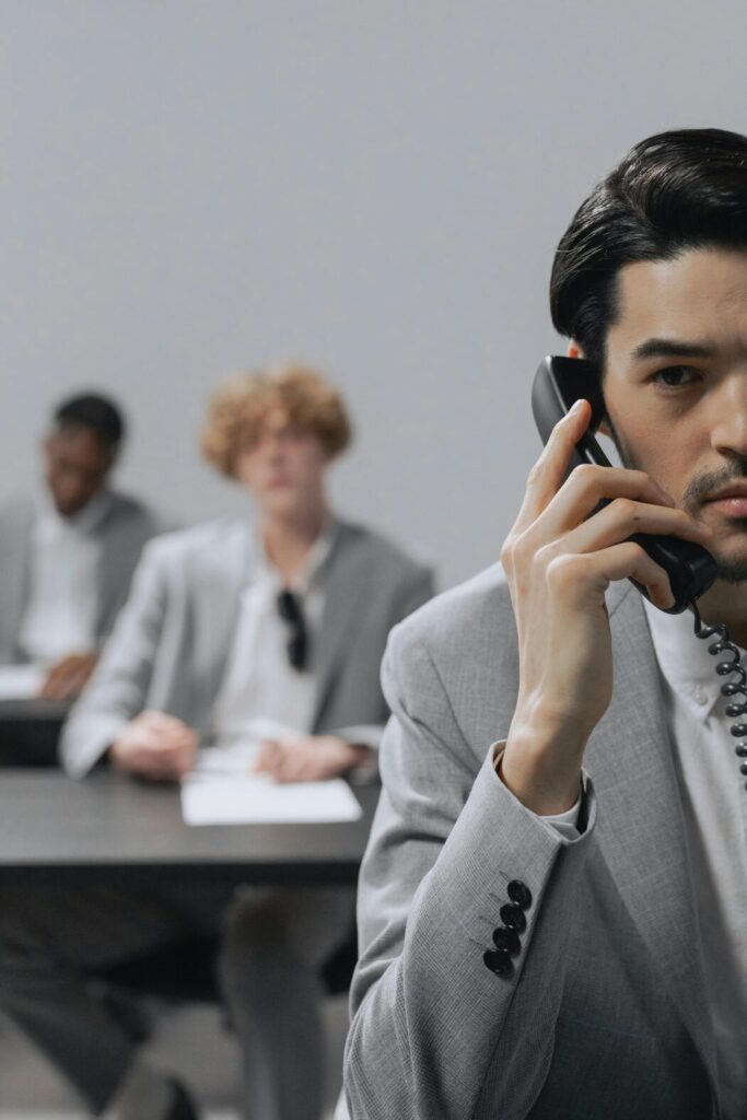 Au premier plan un commercial est au téléphone. Au second et dernier plan, deux autres commerciaux sont à leur bureau
