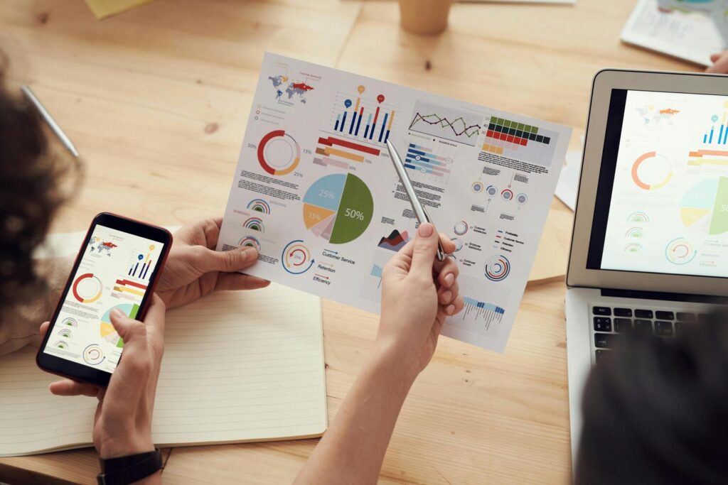 Deux collaborateurs travaillent ensemble sur des outils de suivi de performances d'entreprise. L'un travaille depuis son PC et l'autre partage des donées depuis son smartphone