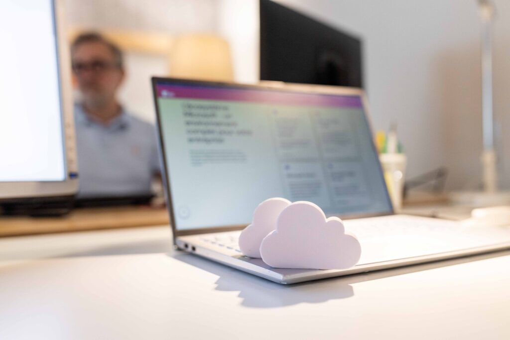 Gros plan sur un laptop ouvert avec deux nuages en mousse posés sur le clavier. A l'écran s'affiche le site web Microsoft et en arrière plan, un membre de l'équipe travaille à son bureau.