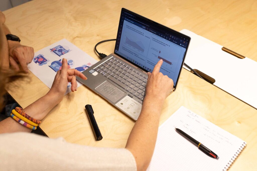 On devine une personne de l'équipe s'adressant à un client assis devant un écran d'ordinateur sur lequel elle pointe des solutions pertinentes pour le client et les spécificités de son activité