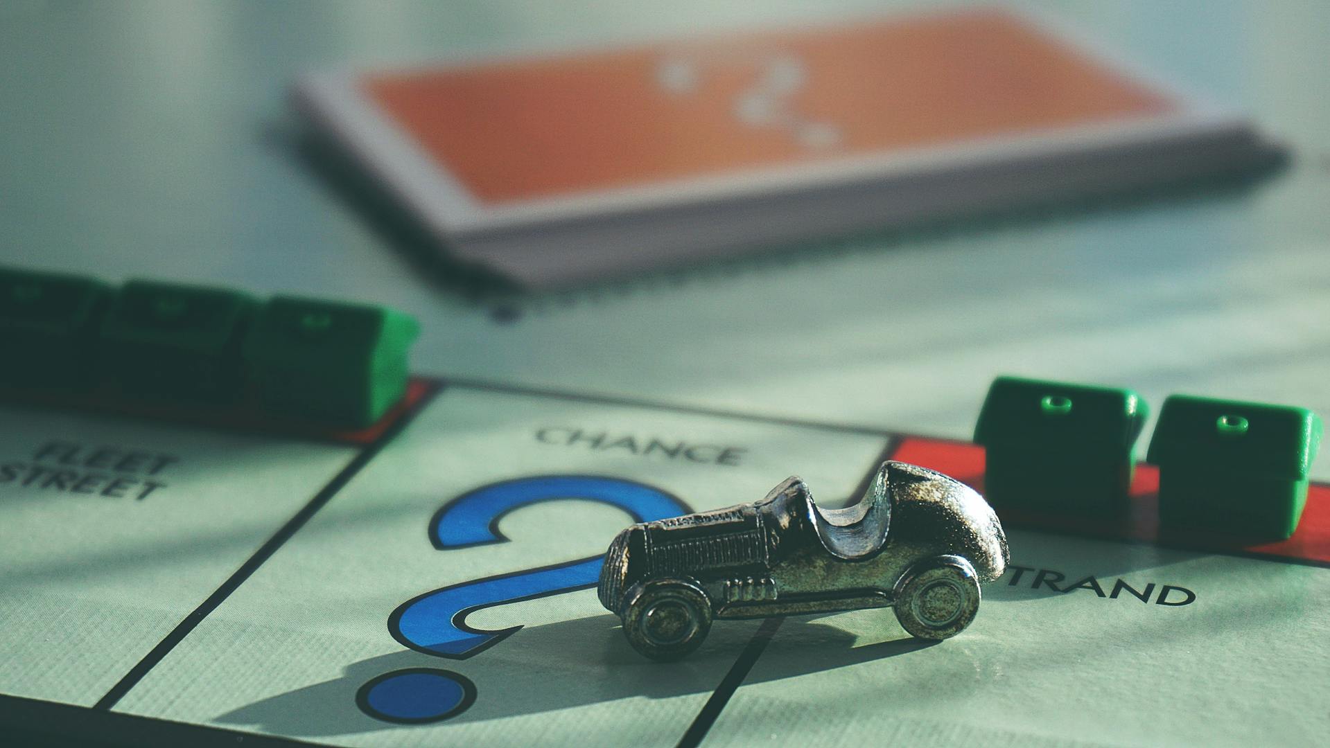 Zoom sur un plateau de Monopoly avec un pion qui avance sur la case chance et le tas de cartes chance en arrière plan.